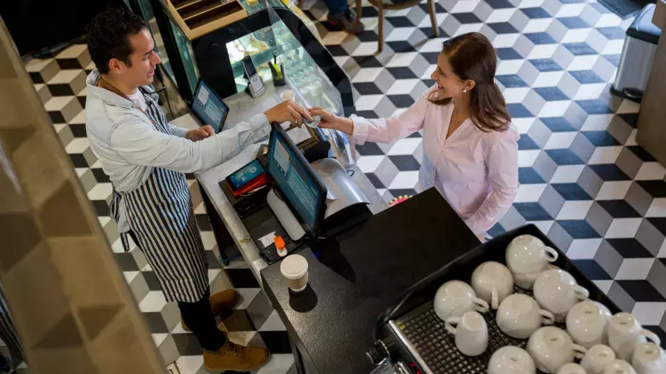 Woman at a cafe buying a cup of coffee to go and paying by cash